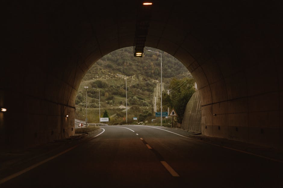 A tunnel opens to a scenic mountain view with a curved road under a muted sky.